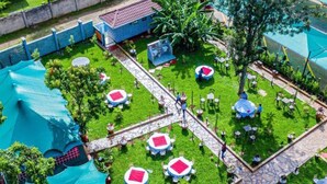 Vue aérienne d’un complexe hôtelier doté d’une piscine, de plusieurs espaces de restauration avec des tables rondes et des parasols, et d’une pelouse bien entretenue.