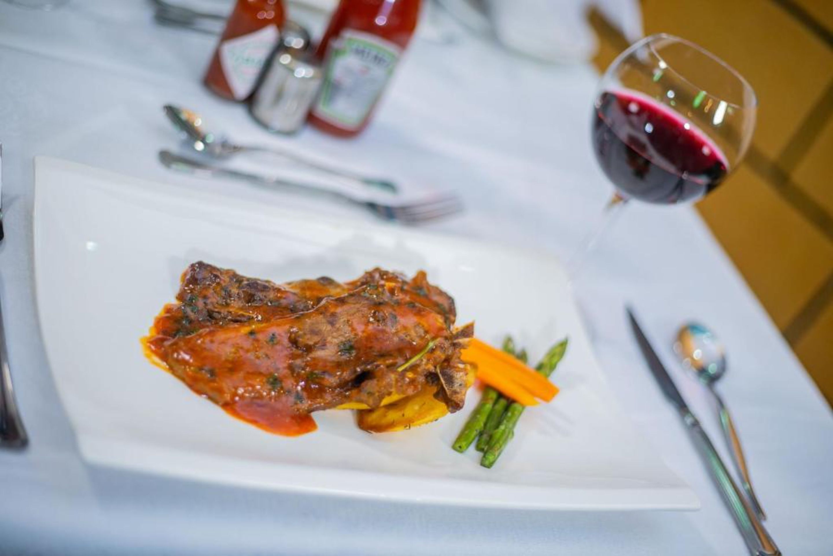Une assiette de nourriture, un verre de vin rouge et des condiments sur une table.