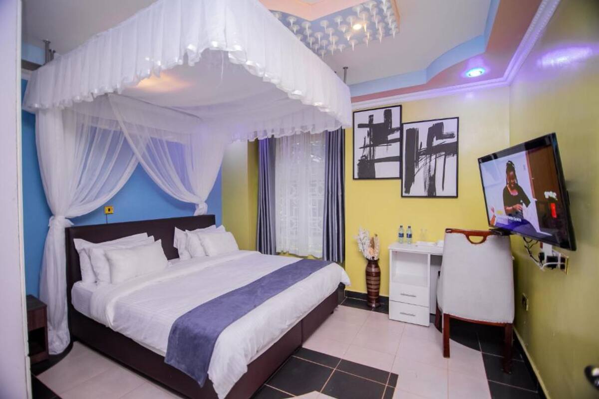 Un dormitorio con cama, escritorio, silla, televisor y obras de arte en las paredes.