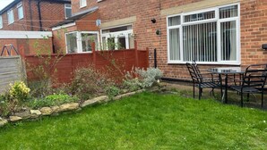 A residential brick house with a front garden, a patio with a table and chairs, and a red fence. - 3 Bed House - Sleeps 5 - Wifi, Parking (Darlington)