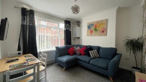 A living room with a blue sofa, a wooden table, and a radiator. - 3 Bed House - Sleeps 5 - Wifi, Parking (Darlington)