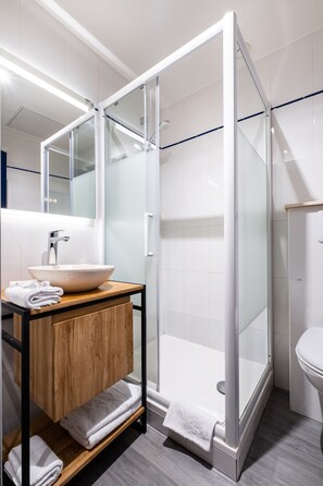 A modern bathroom with a glass-enclosed shower, a wooden vanity, a white sink, and a large mirror. - Hôtel Le Français (La Flotte)