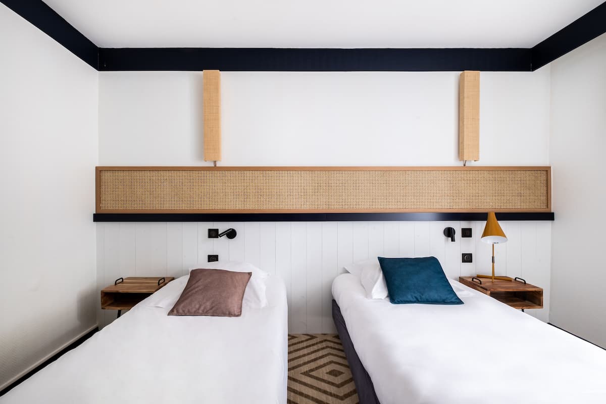 Une chambre d’hôtel avec deux lits, une tête de lit en bois, des tables de chevet et une lampe.