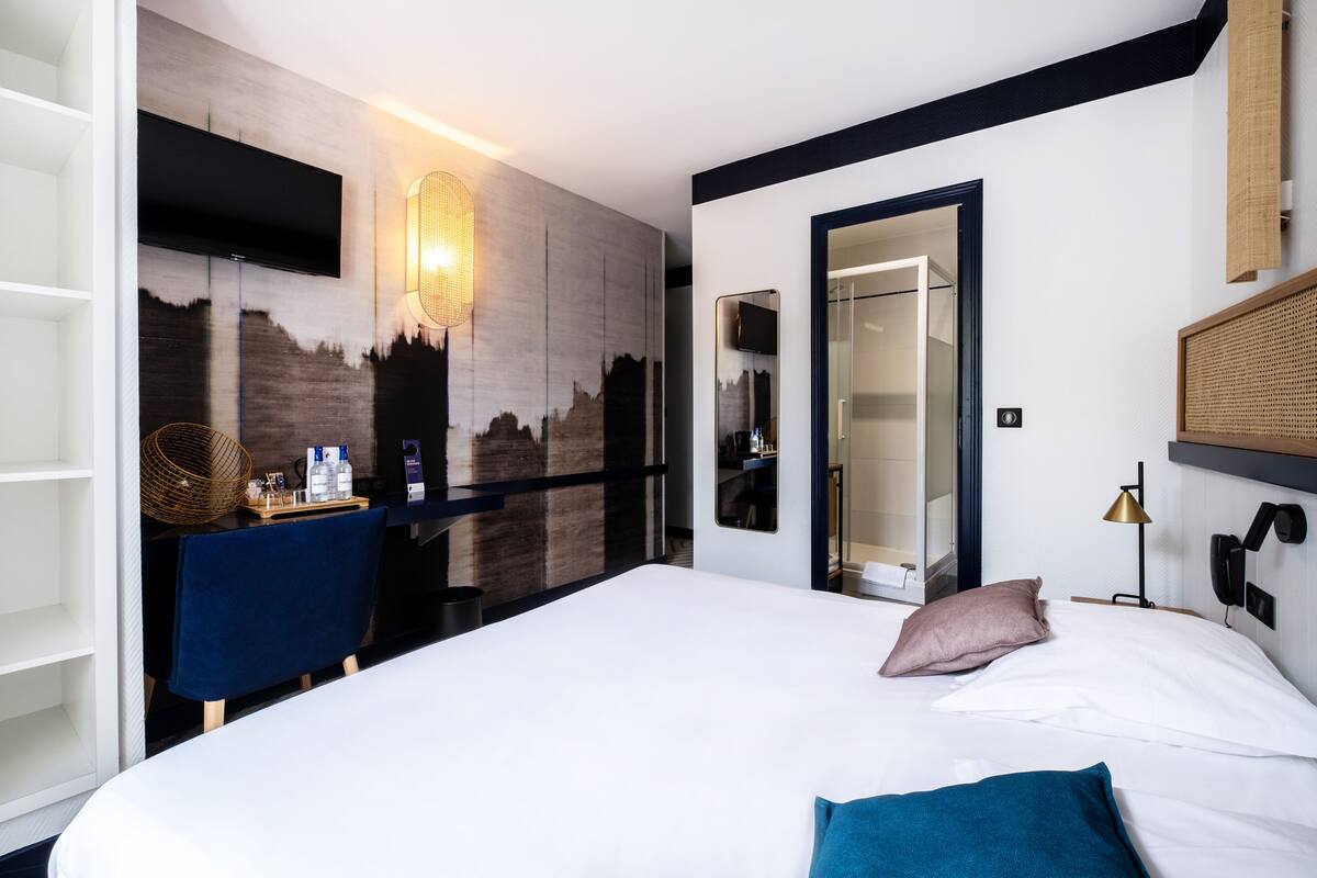 Une chambre d’hôtel moderne dotée d’un grand lit, d’un bureau avec une chaise, d’un téléviseur à écran plat fixé au mur et d’un miroir.