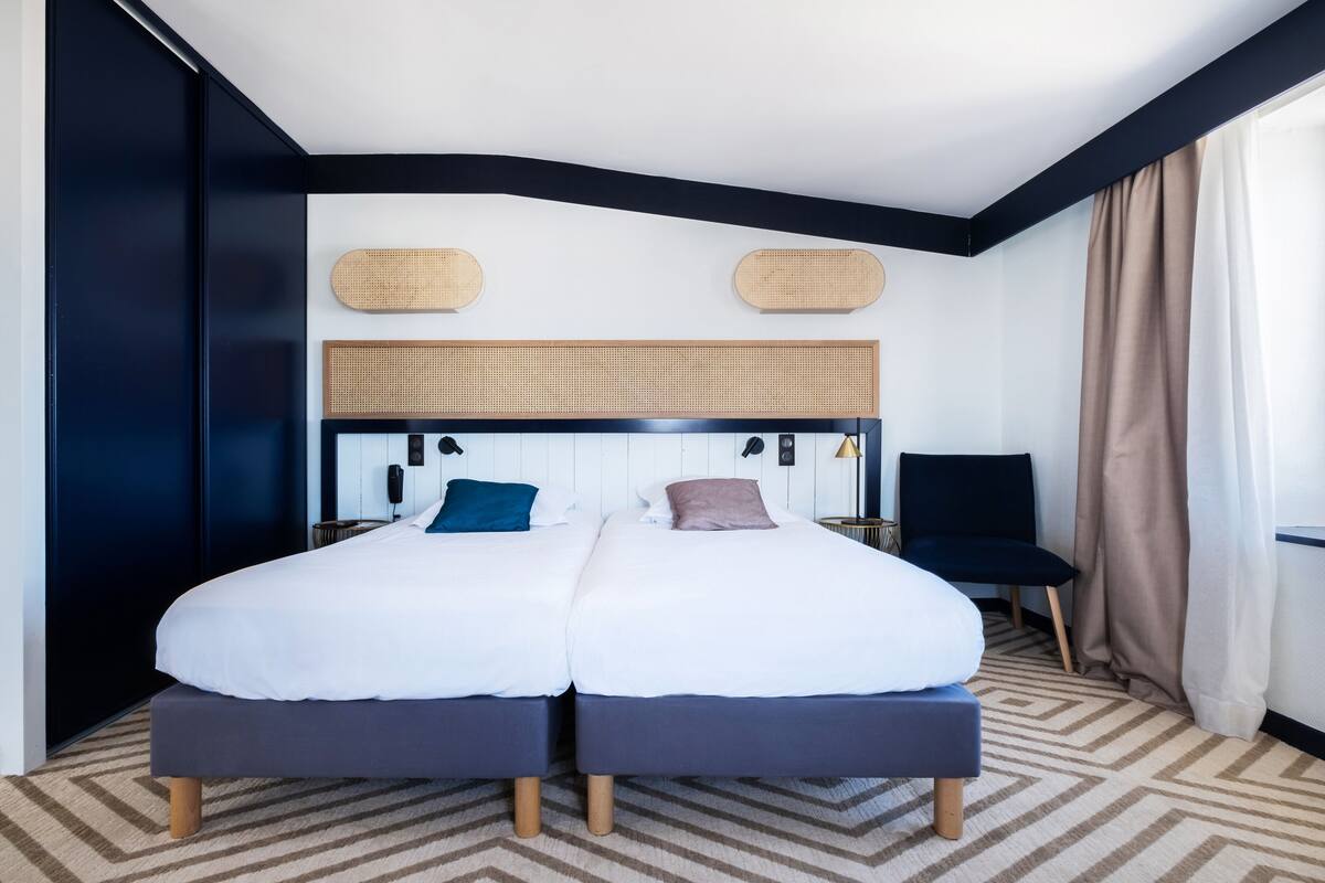 Un lit double avec deux oreillers, une tête de lit ornée de panneaux tissés, une chaise et une fenêtre avec des rideaux.