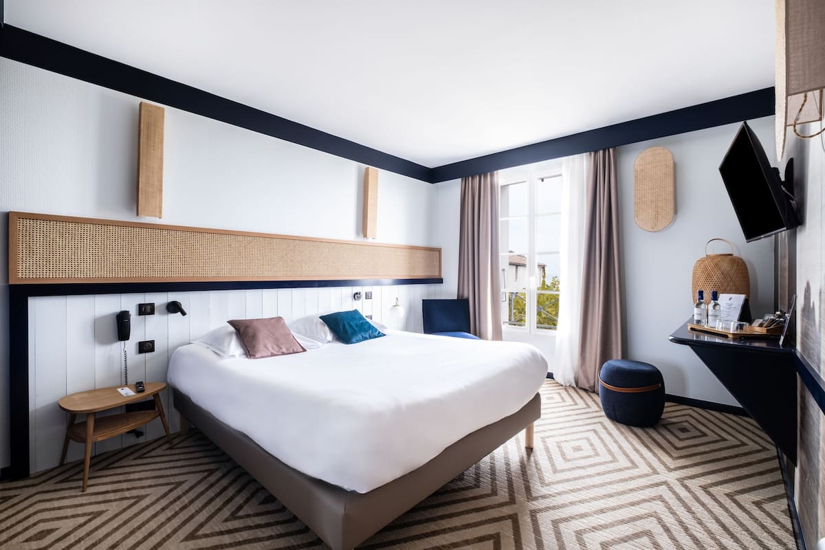 Une chambre d’hôtel avec un grand lit, un bureau avec une chaise, un téléviseur à écran plat et une vue sur l’extérieur.