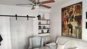 A living room with a sofa, a coffee table, a ceiling fan, a sliding door, and a painting on the wall. - Apartment right on the beach (Playa de Isla Canela)