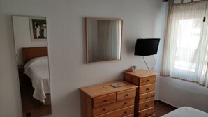 A bedroom with a wooden dresser, a bed, a television, a mirror, and a window with curtains. - Apartment right on the beach (Playa de Isla Canela)
