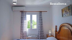 Un dormitori amb un llit, una taula de nit amb una làmpada, una finestra amb cortines i un aparell d'aire condicionat.