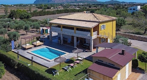 Eine gelbe Villa mit Pool, Sitzgelegenheiten im Freien und Blick auf Berge.
