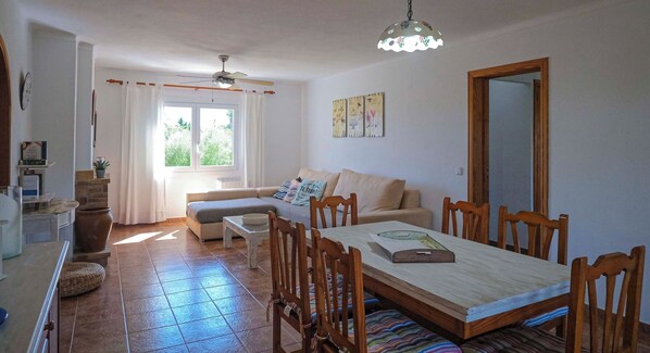Un amplio salón con una mesa de comedor, sillas de madera, un sofá y un ventilador de techo.