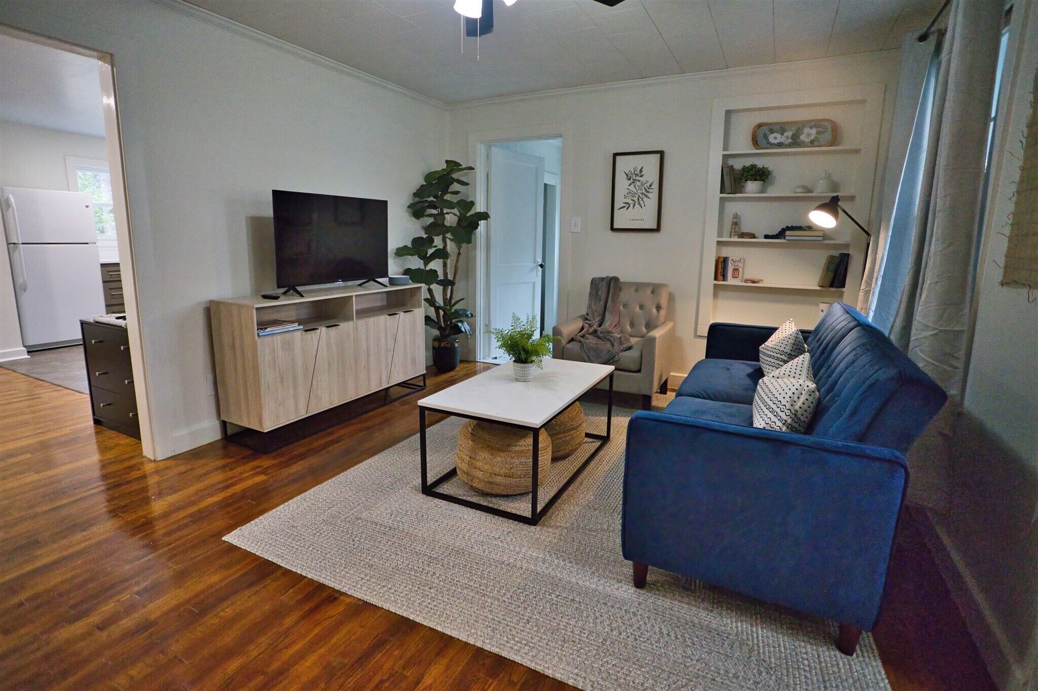 Ett modernt vardagsrum med en blå soffa, ett vitt soffbord och en tv-apparat placerad på ett träskåp.