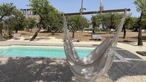 Una hamaca suspendida sobre una piscina, con vista a un edificio y árboles al fondo.