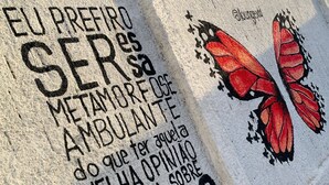 En vägg täckt av graffiti, inklusive en fjäril och text på portugisiska.