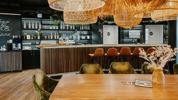 Un área de bar moderna con una mesa de madera, sillas tapizadas en verde y una lámpara de techo de mimbre.