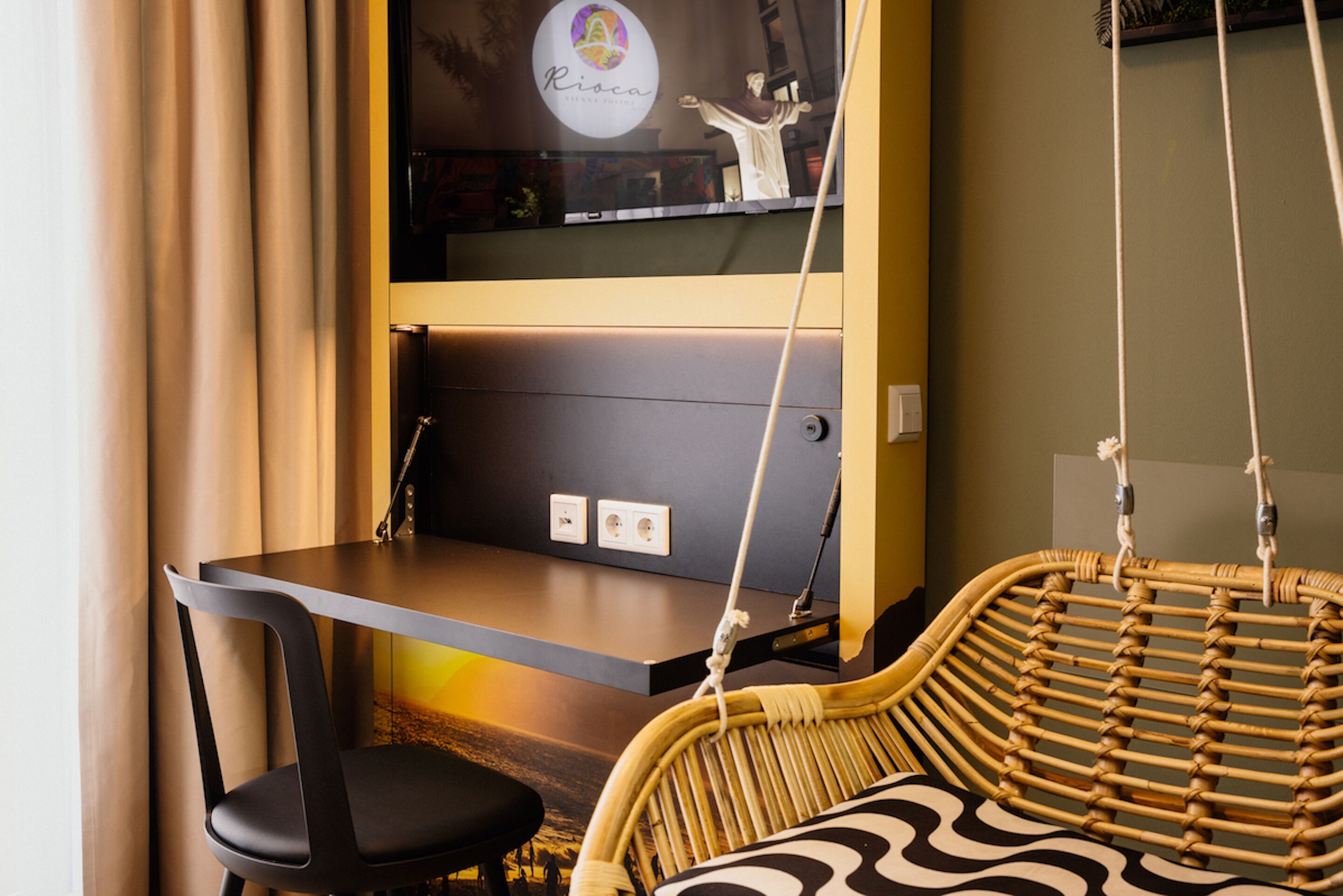 A modern room with a dark wooden desk, a black chair, a wicker chair, and a wall-mounted shelf with a statue and a circular logo.