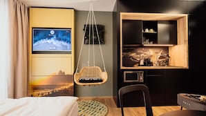Une chambre d’hôtel moderne équipée d’un lit, d’un fauteuil suspendu, d’une table à manger et d’un coin cuisine avec un plan de travail en bois.