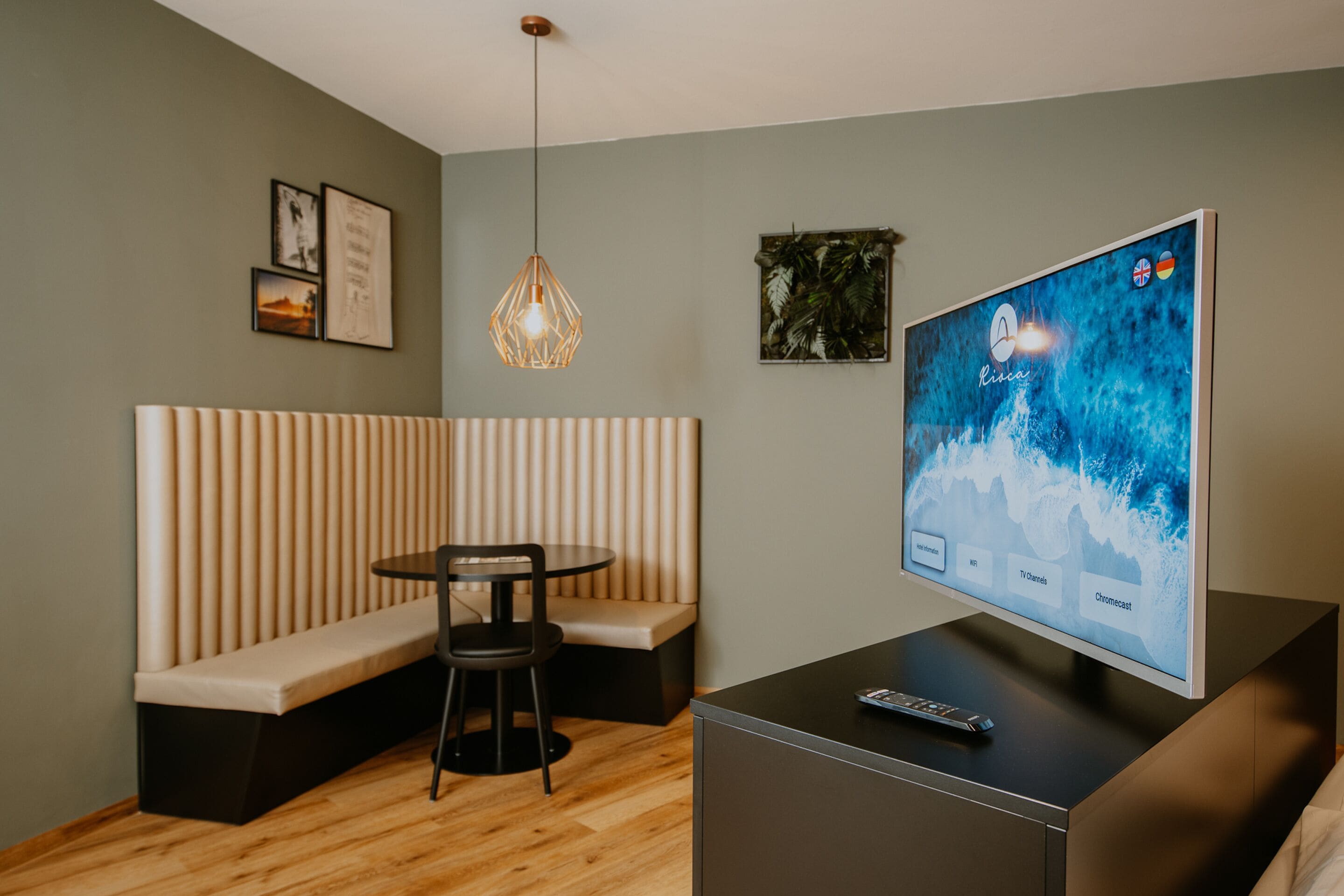 A modern room with a large flat-screen TV, a wooden table, a bench, and a hanging light fixture.