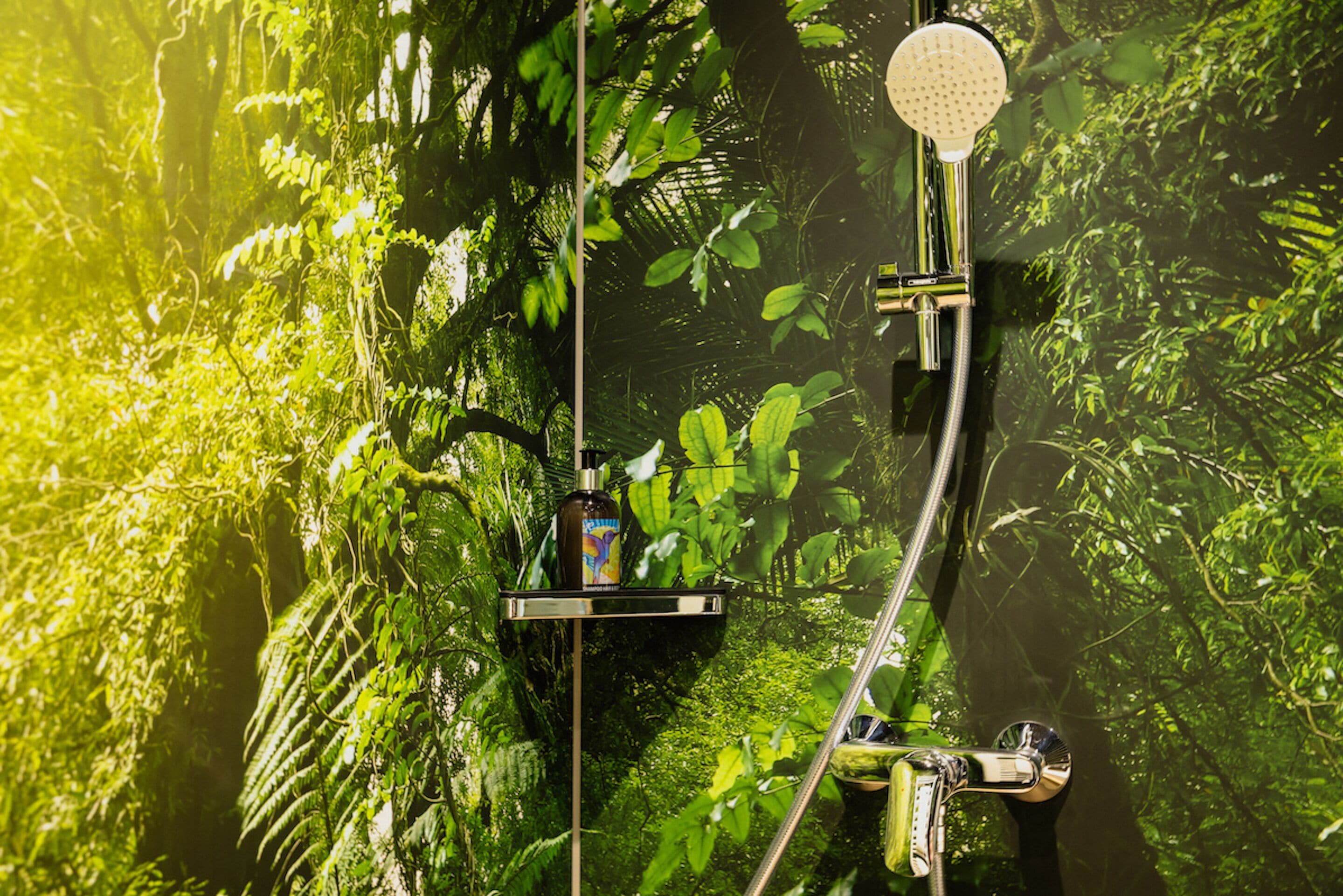 A shower with a handheld showerhead and a bottle of shampoo on a shelf.