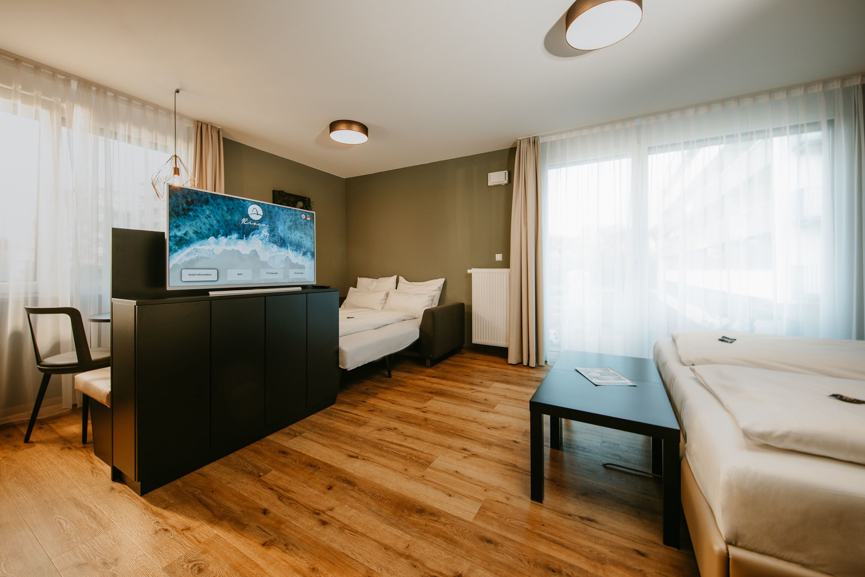 Ein modernes Hotelzimmer mit Holzboden, einem Bett, einer Couch, einem Fernseher und einem Schreibtisch.