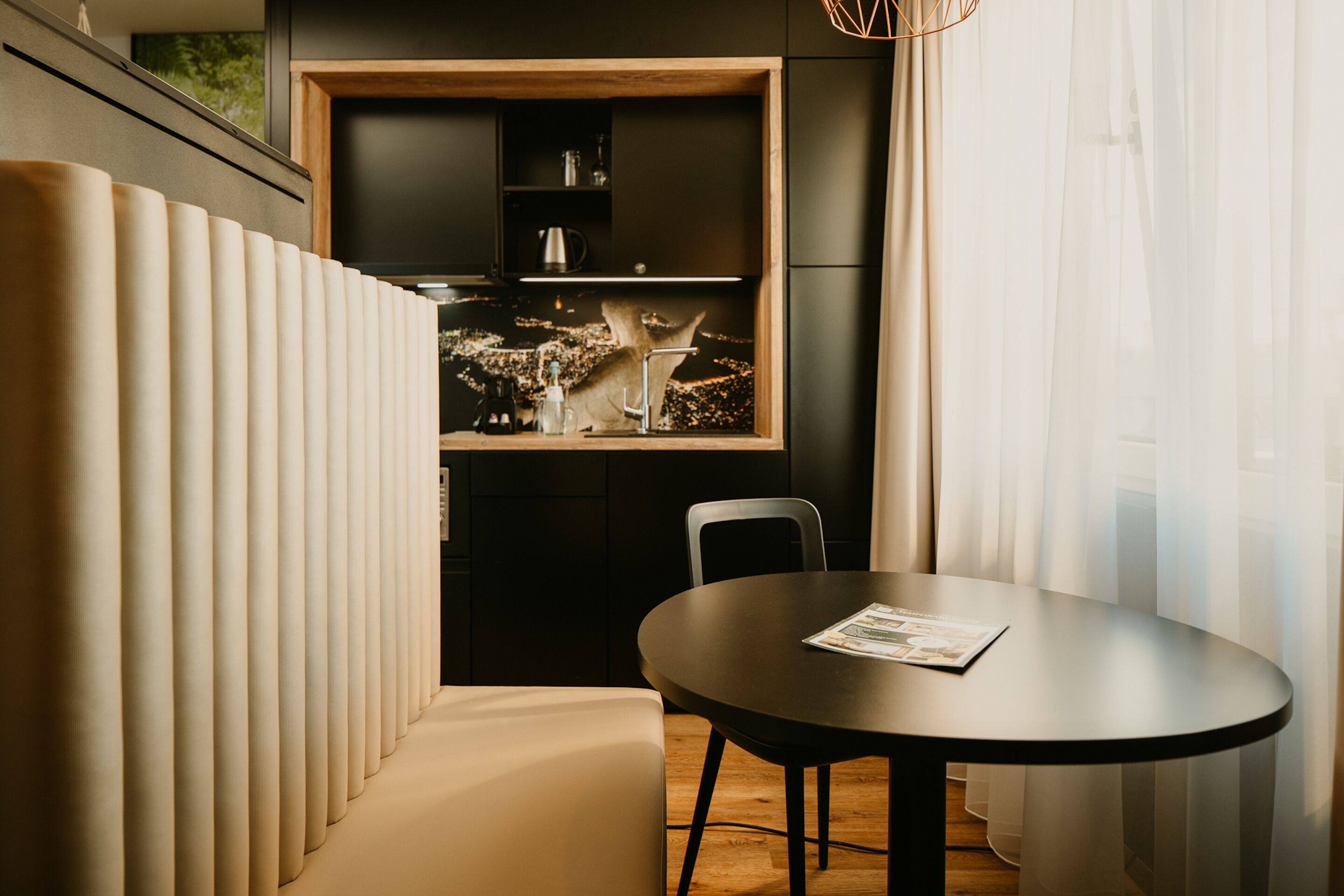 Un comedor moderno con una mesa redonda y sillas, un banco, y una zona de cocina con armarios y un lavamanos.