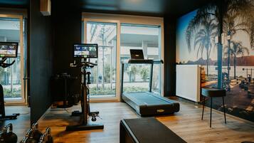 A gym with exercise equipment, a treadmill, and a large window with a view of palm trees and mountains.