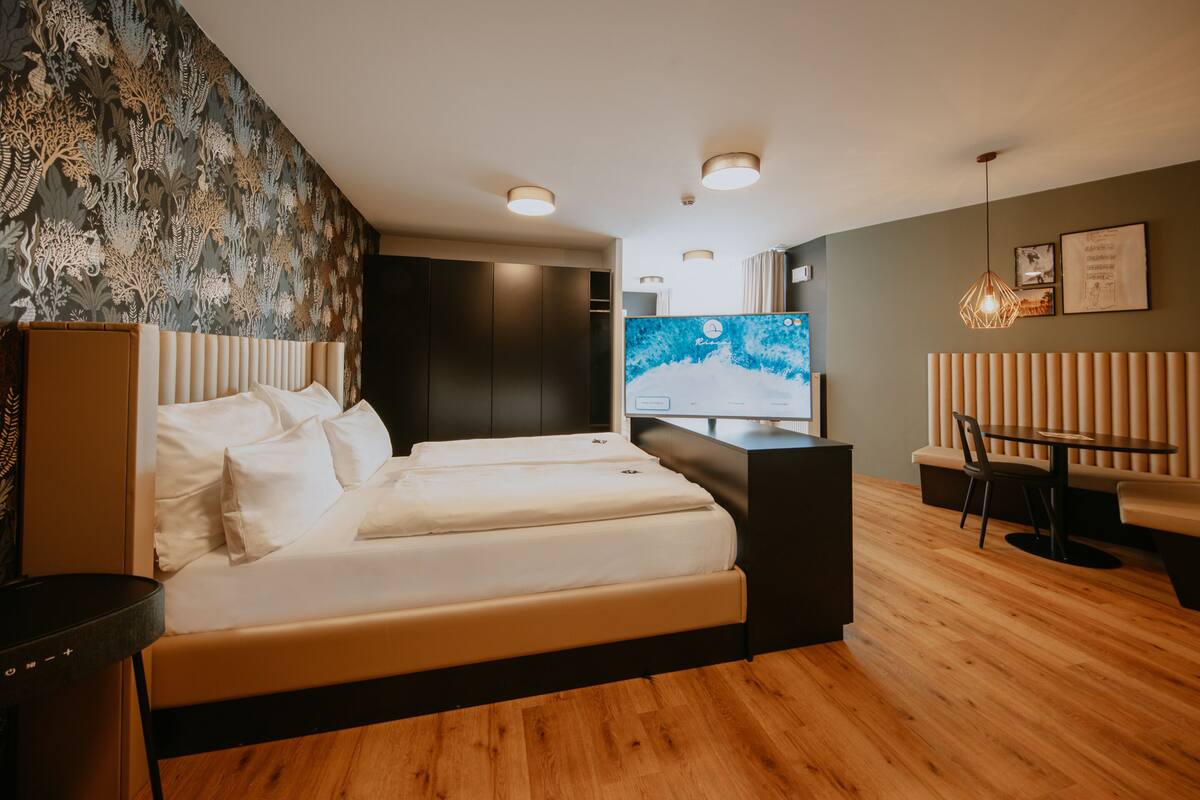 A modern hotel room with a large bed, a desk, a chair, and a television.