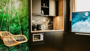 Une cuisine moderne équipée d’un four à micro-ondes encastré, d’un fauteuil suspendu en osier et d’un téléviseur affichant un écran d’informations sur l’hôtel.