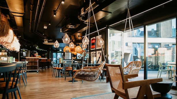 Un intérieur de restaurant moderne avec un plancher en bois, des chaises suspendues en osier et des luminaires suspendus.
