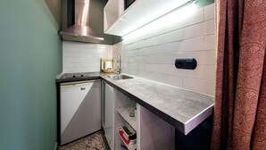 Cocina compacta con armarios blancos, extractor de acero inoxidable, microondas integrado y un lavamanos.