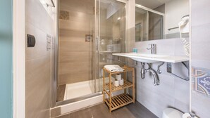 Un baño moderno con ducha envuelta en cristal, un estante de madera con artículos de aseo, un lavabo blanco y un espejo sobre él.