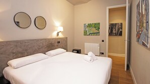 A hotel room with a large bed, two wall-mounted mirrors, a nightstand with a lamp, a painting on the wall, and a door leading to another room.