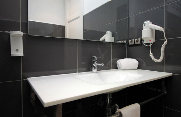 A modern bathroom with a white sink, a mirror, a hairdryer, and a towel rack. - Spacious 2 bedroom apartment with balcony in Eixample, parking possibility (Barcelona)