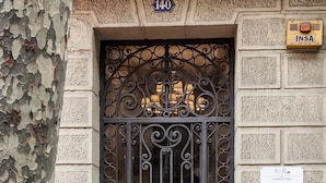 A black wrought iron gate with intricate designs, a number plate '140', and a sign 'INSA' with a phone number.