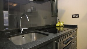 Moderni keittiö, jossa on ruostumattomasta teräksestä valmistettu pesuallas, sisäänrakennettu uuni ja kaasuliesi.