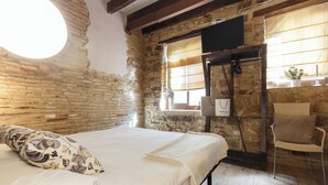 Ein Zimmer mit Bett, Stuhl, einem Vorhangfenster und einer Steinwand.