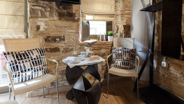 Un coin salon accueillant avec des fauteuils en osier, une petite table ronde agrémentée d’un service à café et un téléviseur fixé à un mur en pierre.