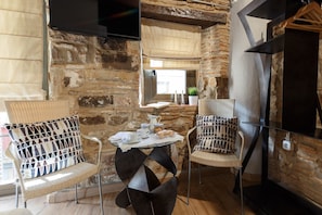 Een gezellig hoekje met rieten stoelen, een klein rond tafeltje met een koffiezet en een televisie bevestigd aan een stenen muur.