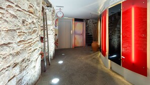 Un couloir aux murs de pierre, avec une horloge et des panneaux rouges rétroéclairés.