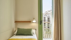 A hotel room with a bed, a nightstand, a lamp, and a view of the outside balcony.