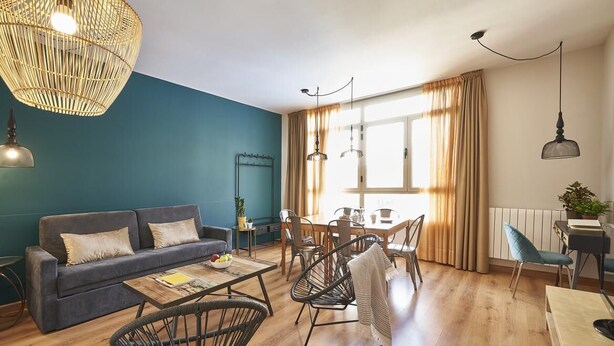 A modern living room with a sofa, dining table, chairs, and a large window with curtains.
