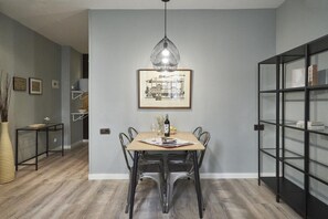 A dining area with a wooden table, metal chairs, a pendant light, and a framed picture on the wall.