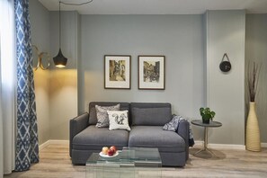 A modern living room with a grey sofa, a glass coffee table, and two framed pictures on the wall.