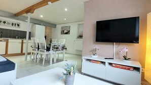 A modern living room with a flat-screen TV, white furniture, and a dining area with chairs and a table. - 3 person vacation apartment in the countryside with plenty of space to linger (Mörlenbach)