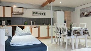 A compact kitchen with modern appliances, a dining area with white chairs, and a bed with patterned bedding. - 3 person vacation apartment in the countryside with plenty of space to linger (Mörlenbach)