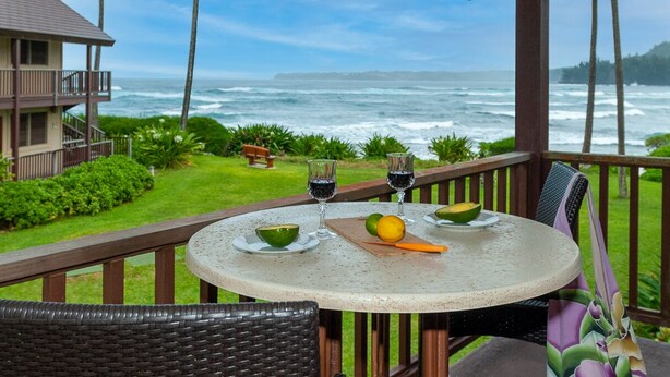 Une table ronde, un verre de vin rouge, un bol de guacamole et une demi-avocat, le tout sur un balcon donnant sur l’océan.