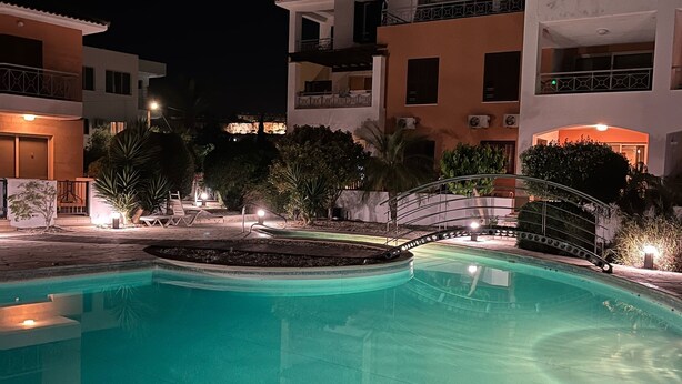 A swimming pool with a tiled deck, surrounded by buildings with balconies and outdoor lighting. - 2 Bedroom Ground Floor Apartment Close to Shops, Restaurants, Old Town and beach (Paphos)