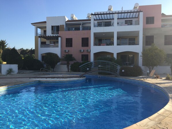 A swimming pool with a bridge, surrounded by a multi-story building with balconies and satellite dishes.