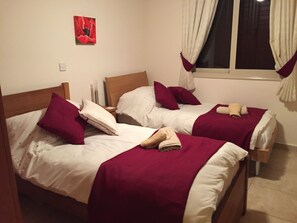 Two single beds with wooden headboards, white bedding, and purple pillows.