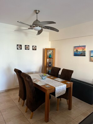 A dining area with a wooden table, four chairs, a ceiling fan, and wall decorations including framed pictures and a vase.